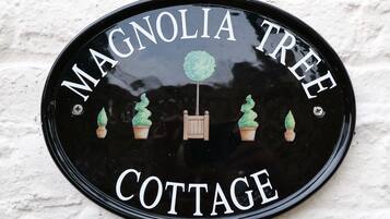 A black circular sign with white lettering stating "Magnolia Tree Cottage."