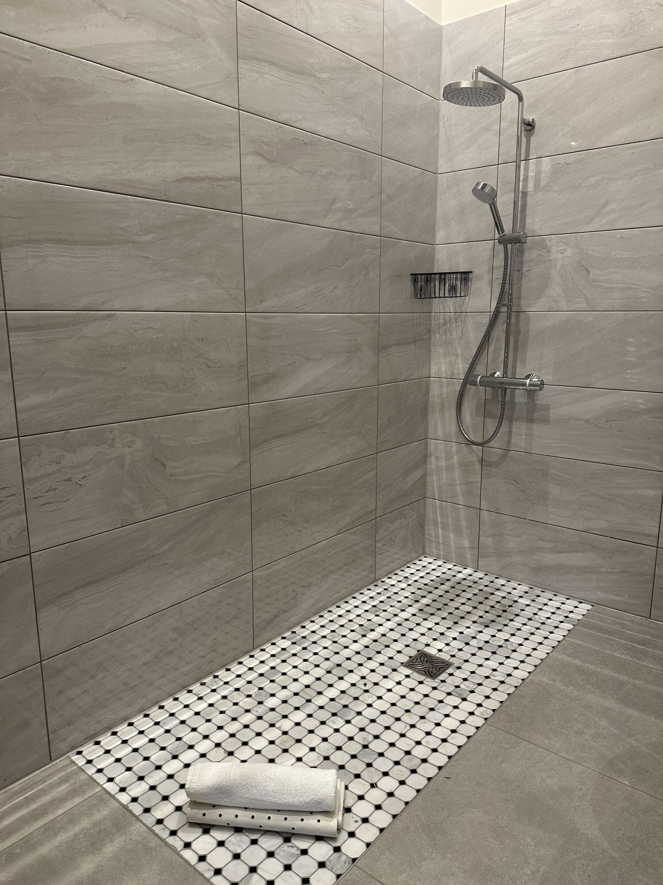 A modern shower area with a rain showerhead, handheld showerhead, and a handheld shower attachment.