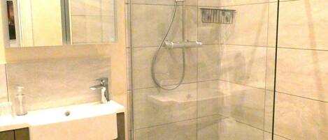 A modern bathroom with a glass-enclosed shower, a sink with a mirror, and a toilet.