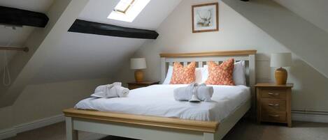 A bedroom with a sloped ceiling, a skylight, a bed with white linens, two nightstands with lamps, and a framed picture on the wall.