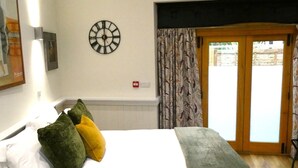 A bedroom with a bed, pillows, a clock, and a view through a door. - The Frocester (Stonehouse)