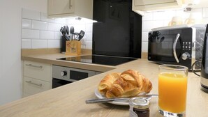A kitchen with a microwave, toaster, and a breakfast setting including croissants and orange juice. - The Frocester (Stonehouse)