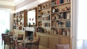 A library with bookshelves, a fireplace, and dining tables with chairs. - The Frocester (Stonehouse)