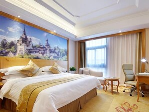 A hotel room with a large bed, a desk, a chair, and a large window with curtains.