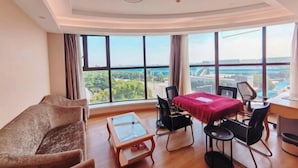 A modern hotel room with a large window offering a city view, a cozy sofa, a dining table with chairs, and a small wooden coffee table. - Vienna International Hotel (Shanghai Songjiang Development Zone Sports Center Metro Station) (Shanghai)