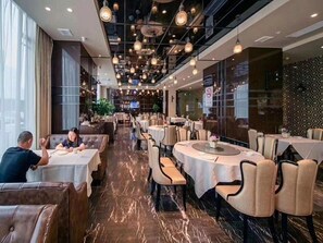 A restaurant with round tables, chairs, and a high ceiling with hanging lights.