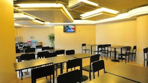 A dining area with multiple tables and chairs, a television mounted on the wall, and a kitchen area in the background. - Vienna Hotel Guangzhou Panyu Changlong Shiqiao Metro Station (Guangzhou)