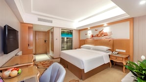 A hotel room with a bed, bedside table, lamp, TV, desk with laptop, chair, and a potted plant. - Vienna Hotel Guangzhou Panyu Changlong Shiqiao Metro Station (Guangzhou)