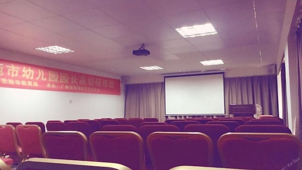 A conference room with rows of red chairs, a projector screen, and a banner on the wall. - Vienna Hotel Guangzhou Panyu Changlong Shiqiao Metro Station (Guangzhou)