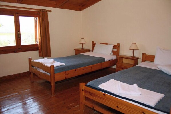 A room with two wooden beds, each with a nightstand and a lamp. There is a window with curtains on the left side. - Pythos Studios & Appartments (Kefalonia)