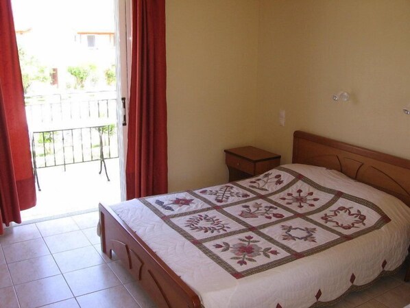A bedroom with a bed, a nightstand, and a window with curtains. - Pythos Studios & Appartments (Kefalonia)