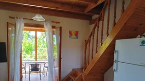 Een kamer met een houten trap, een eethoek met stoelen, een tafel en een koelkast.