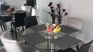 Et moderne spiseområde med et glastilbørsbord omgivet af stole, en vase med blomster og en skål med frugt.