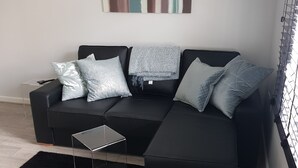 En moderne stue med en hjørnesofa, et glasbord og en sort måtte.