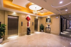 A hotel lobby with two elevators, a chandelier, a red decorative item on the wall, a potted plant, and a framed picture. - Vienna Hotel (Shanghai Jinqiao Park Taierzhuang Road Subway Station) (Shanghai)