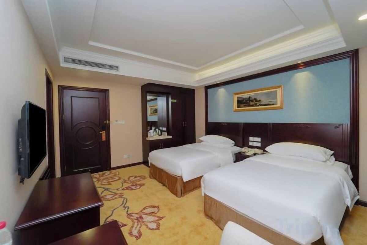 A hotel room with two beds, a television, a desk, and a carpeted floor.