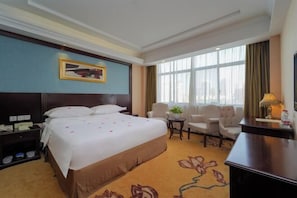 A hotel room with a large bed, a desk, a chair, a small table with a plant, and a window with curtains. - Vienna Hotel (Shanghai Jinqiao Park Taierzhuang Road Subway Station) (Shanghai)