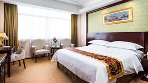 A hotel room with a large bed, two armchairs, a small table with a vase of flowers, and a painting on the wall. - Vienna Hotel (Shanghai Jinqiao Park Taierzhuang Road Subway Station) (Shanghai)