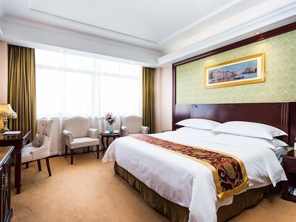 A hotel room with a large bed, two armchairs, a small table with a vase of flowers, and a painting on the wall. - Vienna Hotel (Shanghai Jinqiao Park Taierzhuang Road Subway Station) (Shanghai)