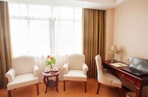 A hotel room with two armchairs, a small round table with a flower vase, a desk with a laptop, and a lamp. - Vienna Hotel (Shanghai Jinqiao Park Taierzhuang Road Subway Station) (Shanghai)
