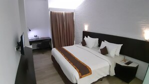 A hotel room with a bed, bedside table, desk, and curtains. - Xtra Bengkulu Managed by Dafam (Bengkulu)