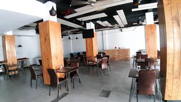 Un amplio comedor interior con altos pilares de madera, mesas y sillas modernas.