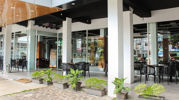 An outdoor seating area with tables and chairs, potted plants, and a glass facade in the background. - Xtra Bengkulu Managed by Dafam (Bengkulu)