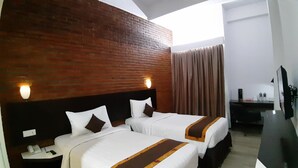 A hotel room with two beds, a brick accent wall, a desk with a chair, and a large window. - Xtra Bengkulu Managed by Dafam (Bengkulu)
