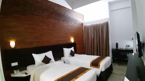Een hotelkamer met twee bedden, een bakstenen muur, een bureau met telefoon en een raam met gordijnen.