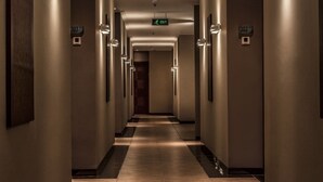 Un pasillo largo e iluminado, con piso de baldosas, flanqueado por paredes con luminarias y letreros de salida.