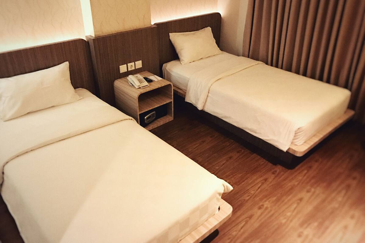 Two single beds with wooden headboards, a nightstand with a phone and a small drawer, and a curtain on the right.