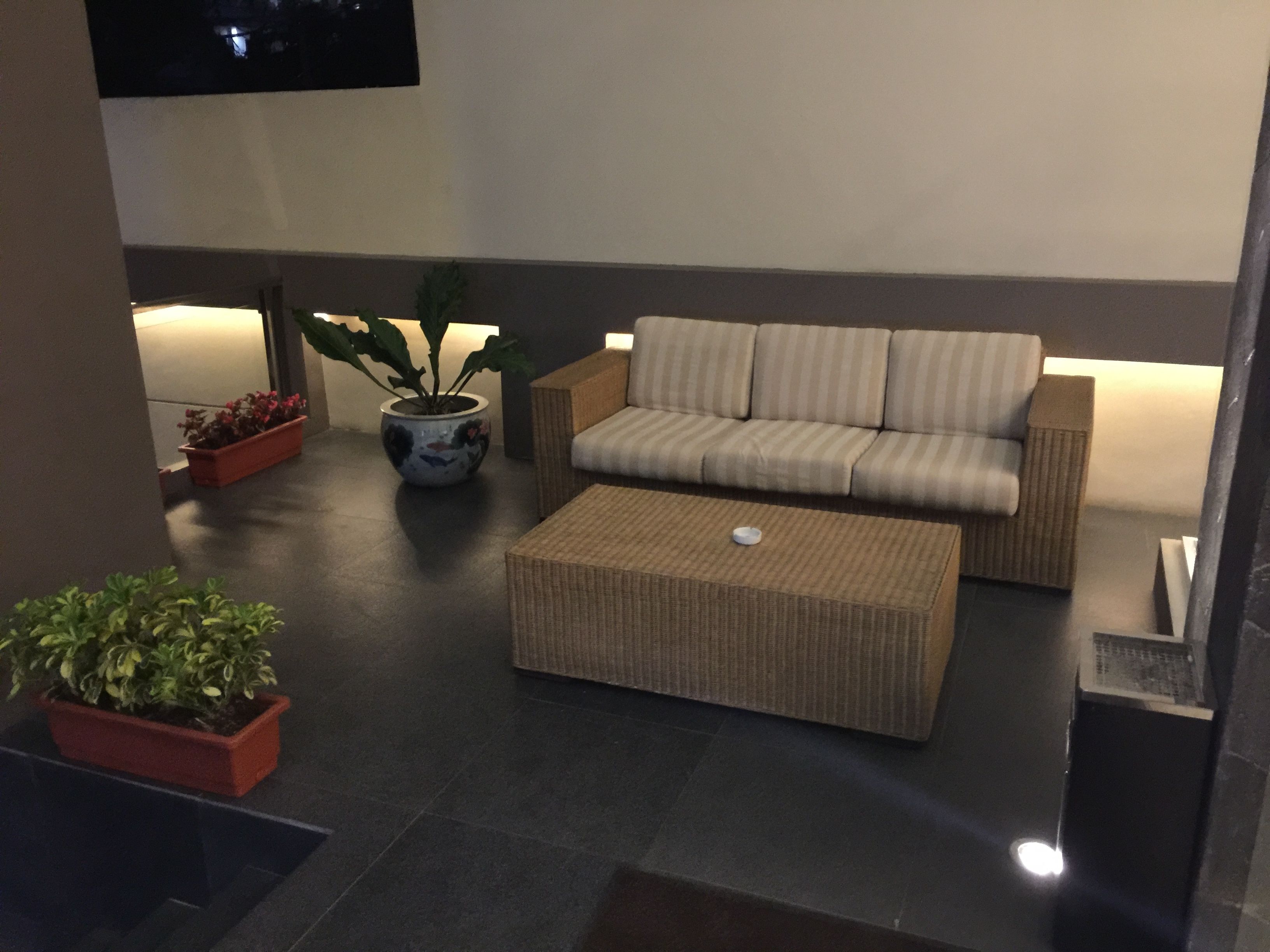 A modern outdoor seating area with a sofa and ottoman, potted plants, and a flat-screen TV mounted on the wall.