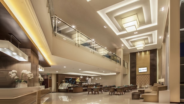 Un moderno hall de hotel con una amplia zona de estar, una recepción y un nivel superior con barandilla de vidrio.