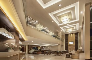 Un moderno hall de hotel con una amplia zona de estar, una recepción y un nivel superior con barandilla de vidrio.