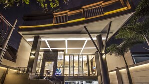 Una entrada de hotel moderna con fachada de vidrio, una escalera visible y un letrero que indica el nombre.