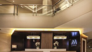 Un moderno vestíbulo de hotel con un mostrador de recepción, una barandilla de vidrio en el nivel superior y un tragaluz.