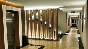 Pasillo de hotel de diseño moderno, con un ascensor central, una escalera y un largo pasillo con piso estampado.