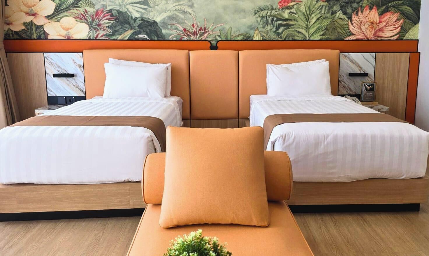 A hotel room with two beds, a wooden headboard, and a mural of tropical flowers.