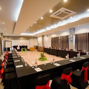 A conference room with a long table, chairs with red sashes, a projector screen, and a clock on the wall. - Sabda Alam Hotel & Resort (Garut)