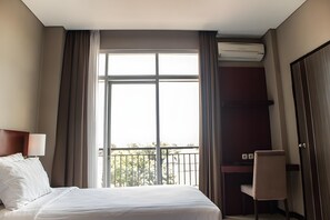 A hotel room with a bed, a desk, a chair, a window with curtains, and an air conditioning unit.
