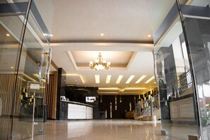 A hotel lobby with a reception desk, a chandelier, and a staircase.