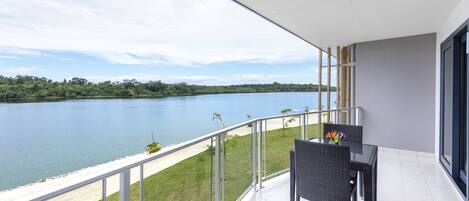 Balcón con vista a un lago y una playa, con una mesa y sillas.