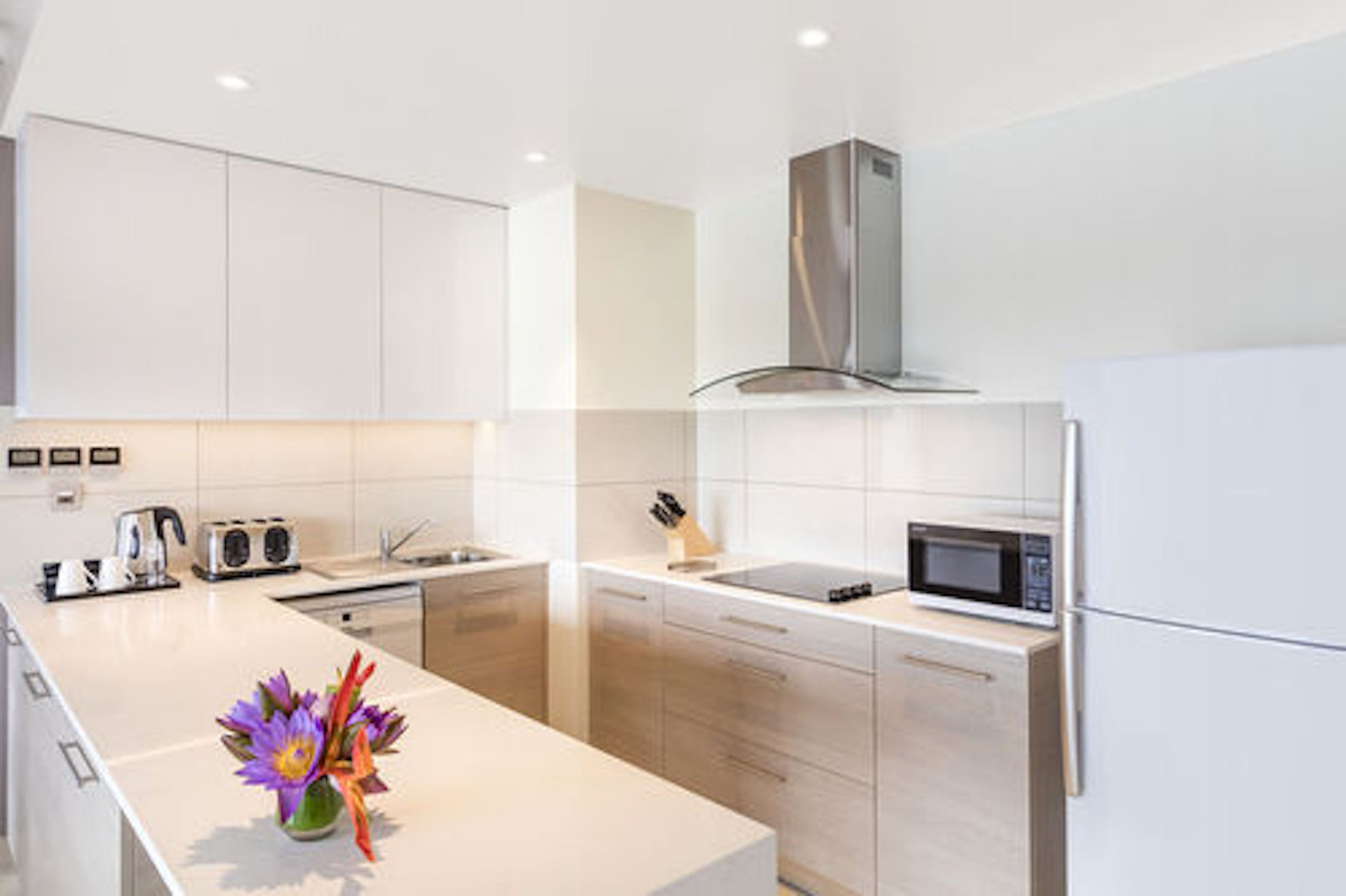 Una cocina moderna con armarios blancos, una campana extractora de acero inoxidable, microondas y cafetera.