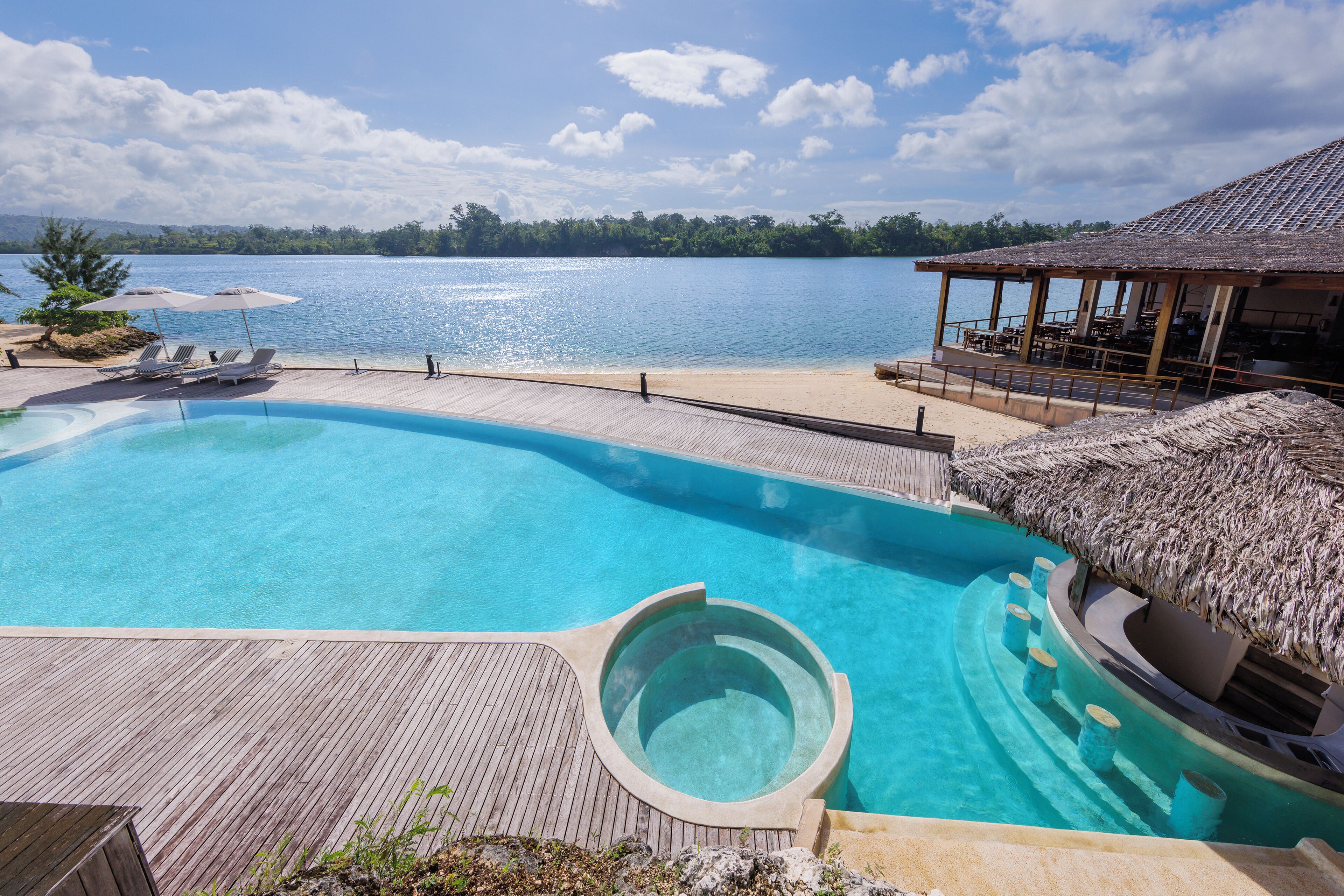 Una piscina con cubierta de madera y un jacuzzi, con vista a un cuerpo de agua.