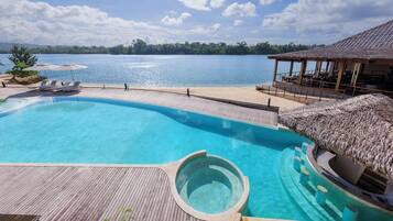 Una piscina con cubierta de madera y un jacuzzi, con vista a un cuerpo de agua.