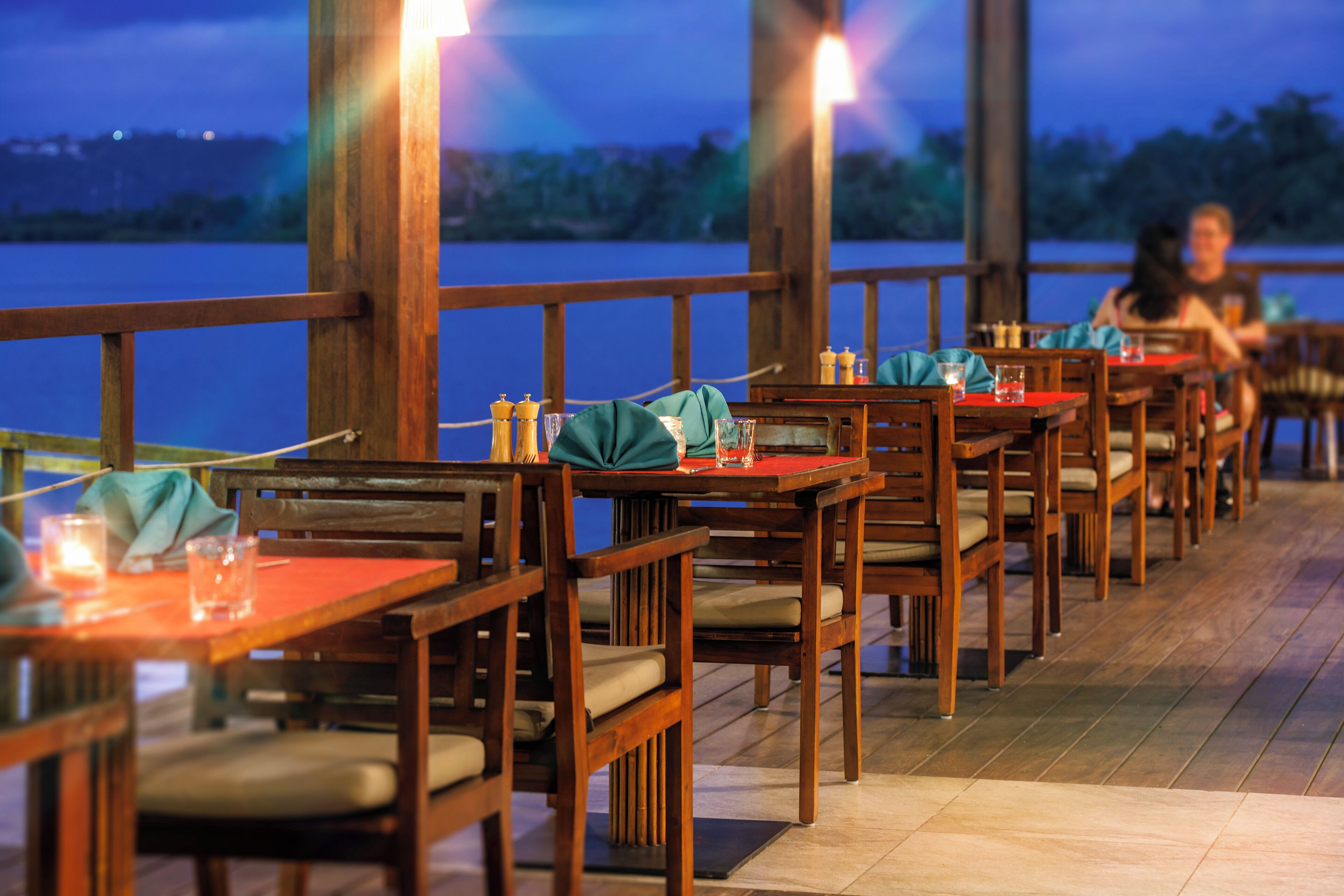 Un restaurante con mesas y sillas de madera, vista al agua y una terraza de madera.