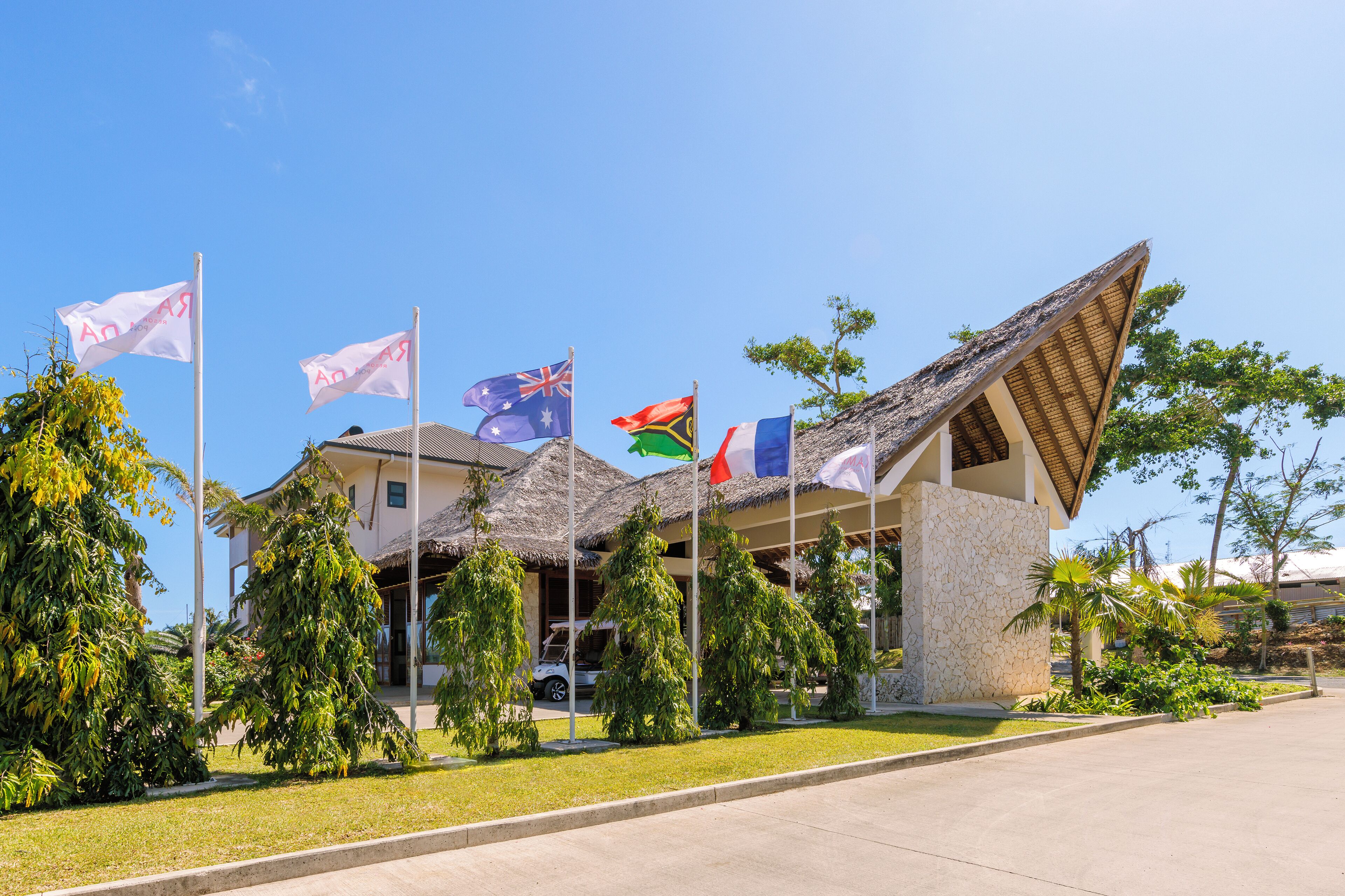 A building with multiple flags, a thatched roof, and a stone facade.