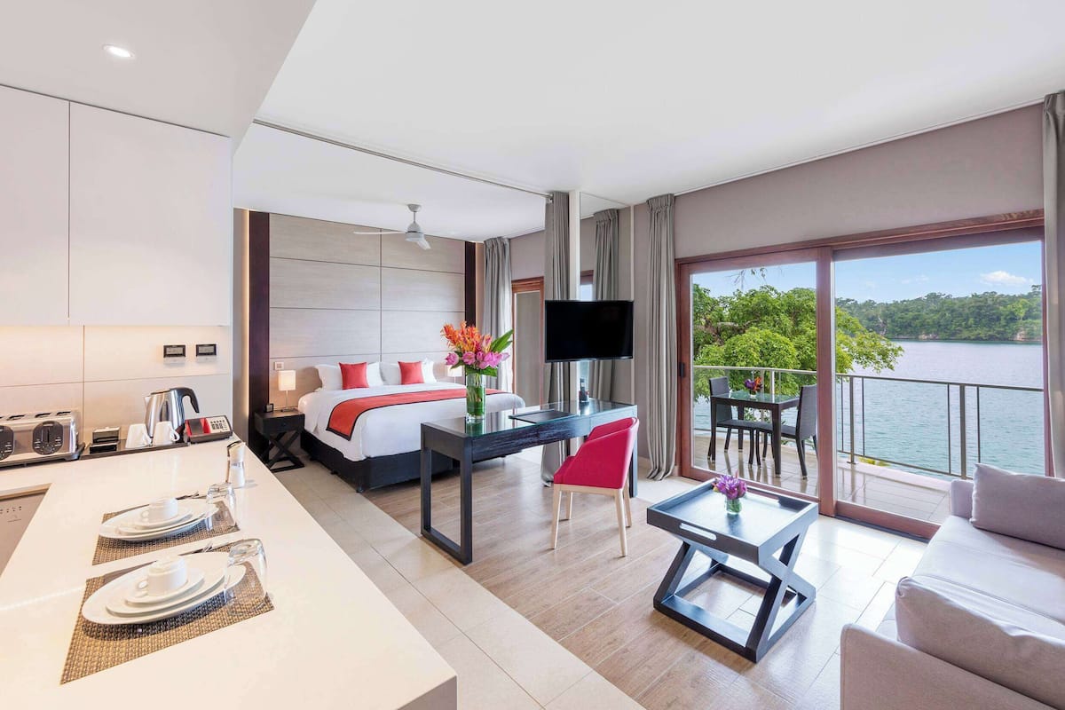 Ein modernes Hotelzimmer mit einem großen Bett, einer Essecke, einem Fernseher und einem Balkon mit Seeblick.