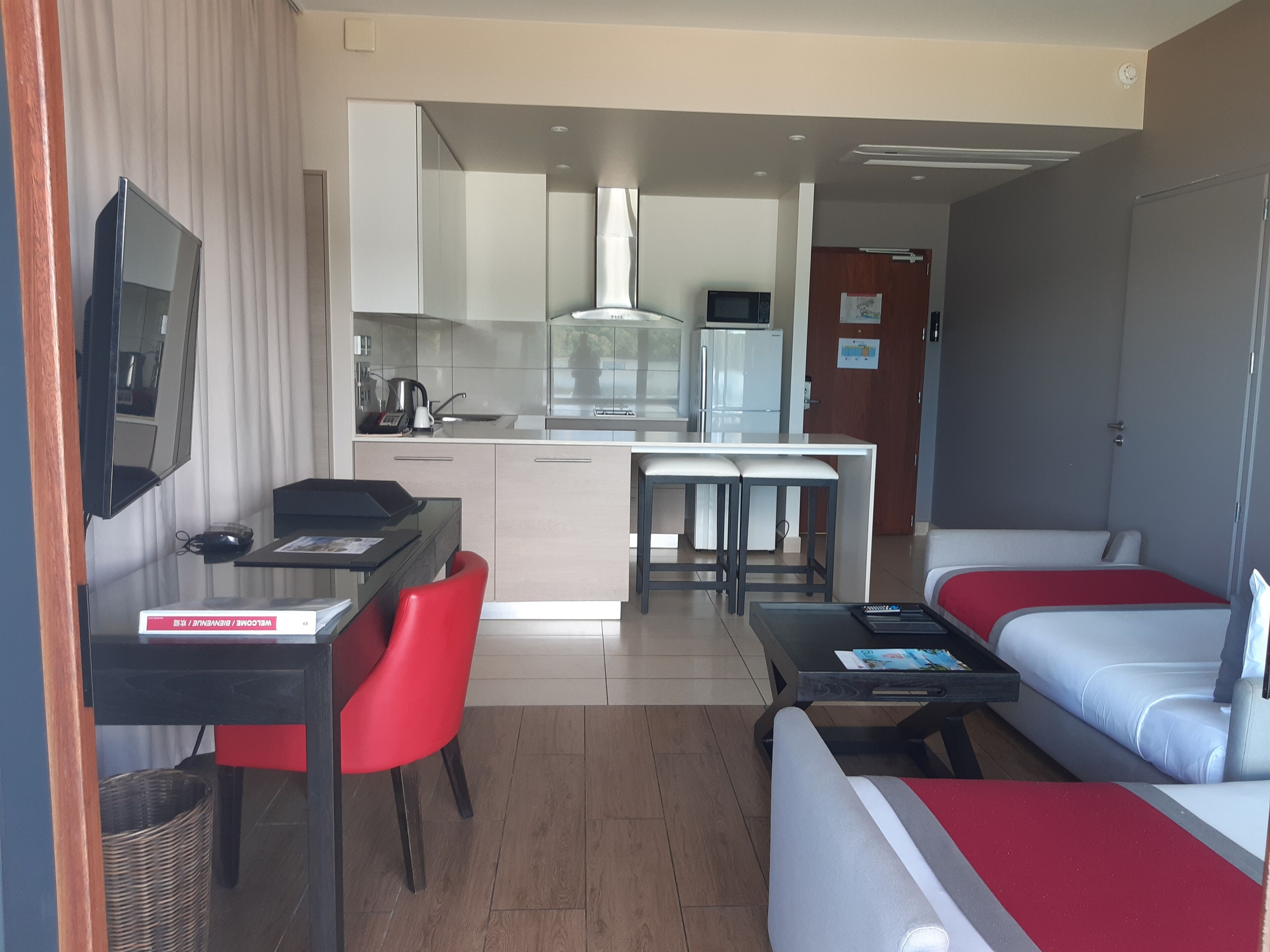A compact hotel room with a kitchenette, a dining area, and a seating area with a sofa and a bed.