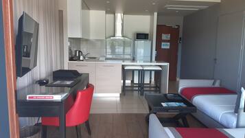 A compact hotel room with a kitchenette, a dining area, and a seating area with a sofa and a bed.